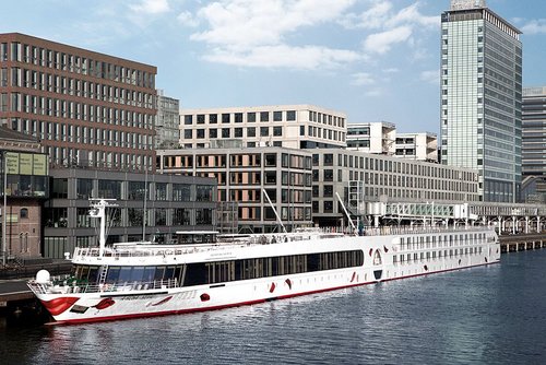 Die A-ROSA SILVA liegt tagsüber in einem Hafen vor modernen Bürogebäuden und Hochhäusern in städtischer Umgebung.