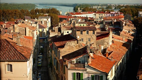 Blick auf die Dächer von Arles mit roten Ziegeln, schmalen Straßen und dem Fluss Rhône im Hintergrund.