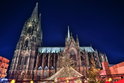 Kölner Dom bei Nacht mit beleuchtetem Weihnachtsmarkt und festlich geschmücktem Weihnachtsbaum im Vordergrund.