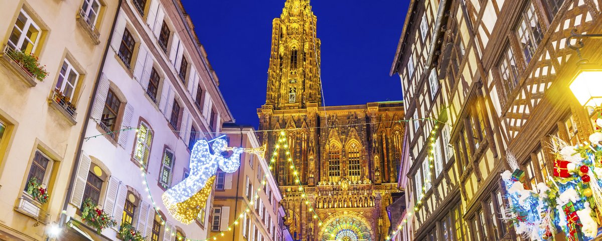 Nächtlicher Blick auf die Kathedrale in Straßburg durch eine Gasse zur Weihnachtszeit. Die Gasse ist festlich beleuchtet.