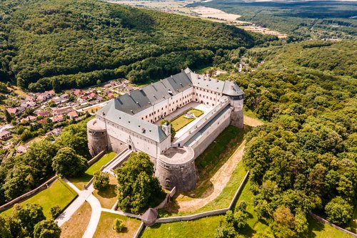 Luftansicht von Burg Červený Kameň in der Slowakei auf einem Hügel, umgeben von weitläufigen Wäldern und Wohnhäusern.