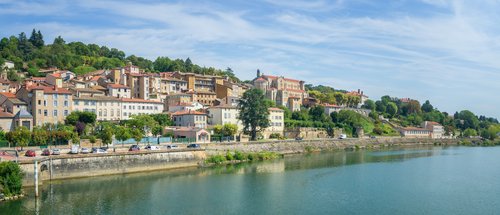 Blick auf die malerische Stadt Trevoux am Ufer der Rhône, mit historischen Gebäuden und grünen Hügeln im Hintergrund.