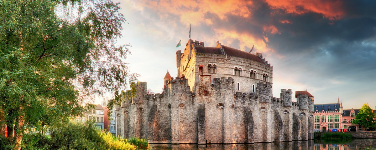 Burg Gravensteen in Gent, Belgien, mit mittelalterlicher Architektur und Türmen, umgeben von Wassergraben und Bäumen.