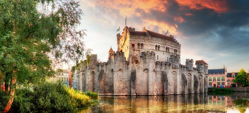 Burg Gravensteen in Gent, Belgien, mit mittelalterlicher Architektur und Türmen, umgeben von Wassergraben und Bäumen.