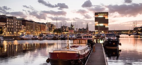 Hafen in Antwerpen bei Abenddämmerung. IM Hafen liegen historische Boote und Yachten. Im Hintergrund historische und moderne Gebäude