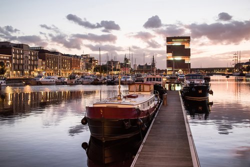 Hafen in Antwerpen bei Abenddämmerung. IM Hafen liegen historische Boote und Yachten. Im Hintergrund historische und moderne Gebäude