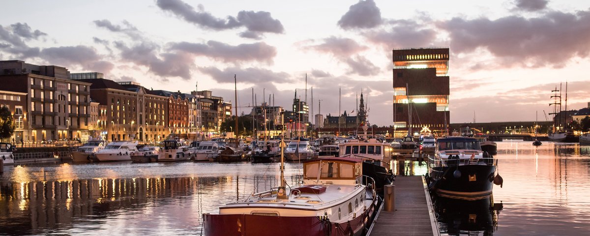 Hafen in Antwerpen bei Abenddämmerung. IM Hafen liegen historische Boote und Yachten. Im Hintergrund historische und moderne Gebäude