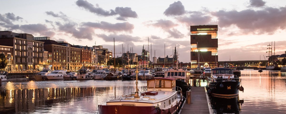 Hafen in Antwerpen bei Abenddämmerung. IM Hafen liegen historische Boote und Yachten. Im Hintergrund historische und moderne Gebäude
