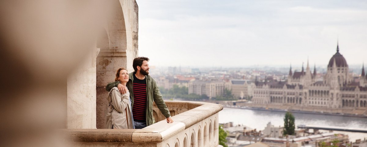 Ein Paar genießt den Ausblick von der Fischerbastei in Budapest, mit Blick auf das ungarische Parlament und die Donau im Hintergrund.
