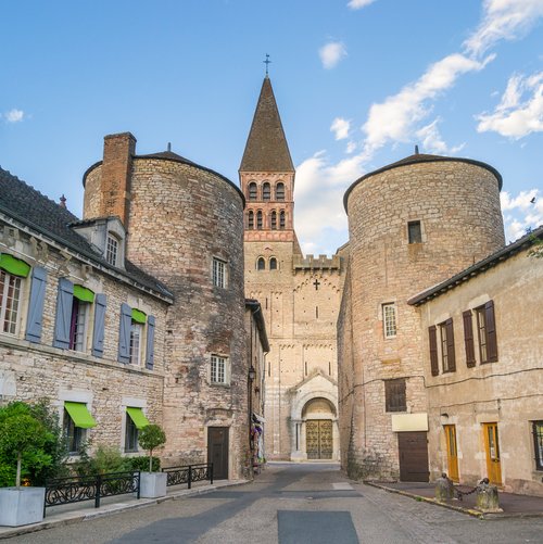 Eine malerische Stadtansicht von Tournus mit der romanischen Abteikirche Saint-Philibert und umliegenden historischen Gebäuden bei blauem Himmel.