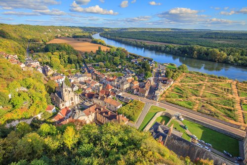Luftaufnahme der Stadt La Roche-Guyon mit typischen fanzösischen Häusern und einer kleinen Kirche am Flussufer.