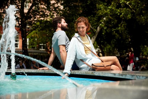 Ein Paar sitzt auf einem Springbrunnen in Bratislava, umgeben von Bäumen und anderen Menschen im Hintergrund.