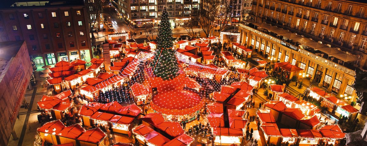 Weihnachtsmarkt in Köln bei Nacht mit festlich beleuchteten Ständen, einem großen Weihnachtsbaum und Menschen, die durch den Markt schlendern.