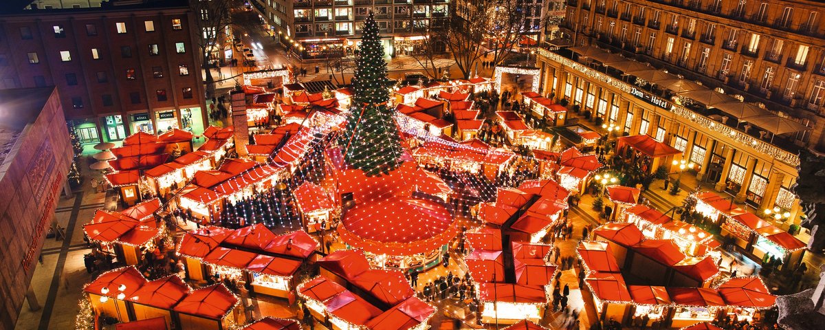 Weihnachtsmarkt in Köln bei Nacht mit festlich beleuchteten Ständen, einem großen Weihnachtsbaum und Menschen, die durch den Markt schlendern.