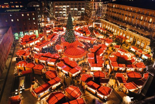 Weihnachtsmarkt in Köln bei Nacht mit festlich beleuchteten Ständen, einem großen Weihnachtsbaum und Menschen, die durch den Markt schlendern.