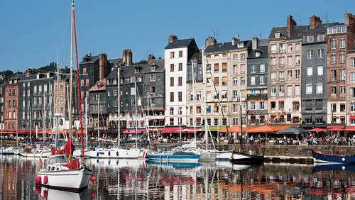 Hafen von Caudebec-en-Caux mit Segelbooten vor historischen mehrstöckigen Häusern und belebten Cafés am Ufer