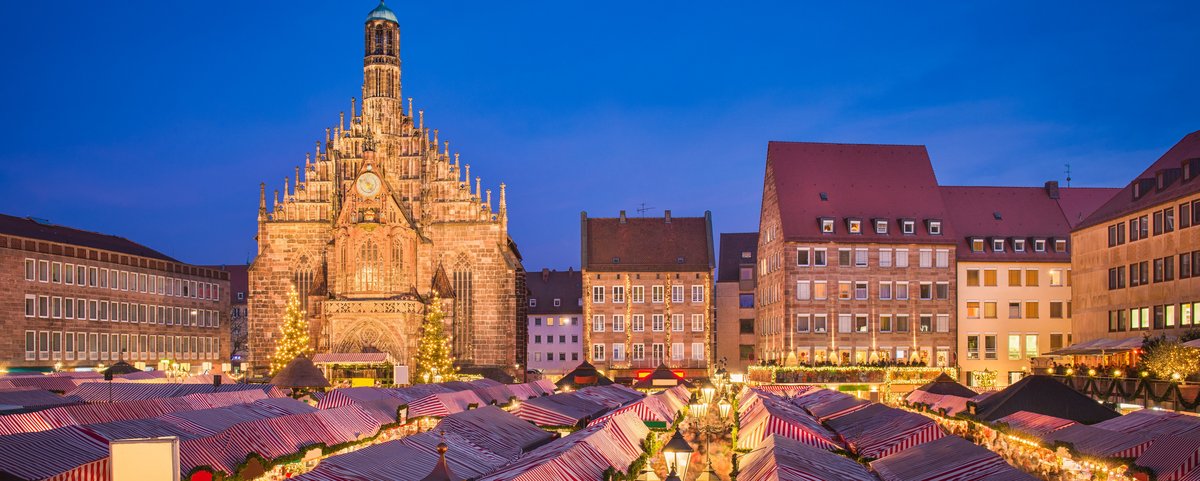 Weihnachtsmarkt in Nürnberg bei Nacht, mit festlich beleuchteten Ständen und einem großen, geschmückten Weihnachtsbaum im Hintergrund.