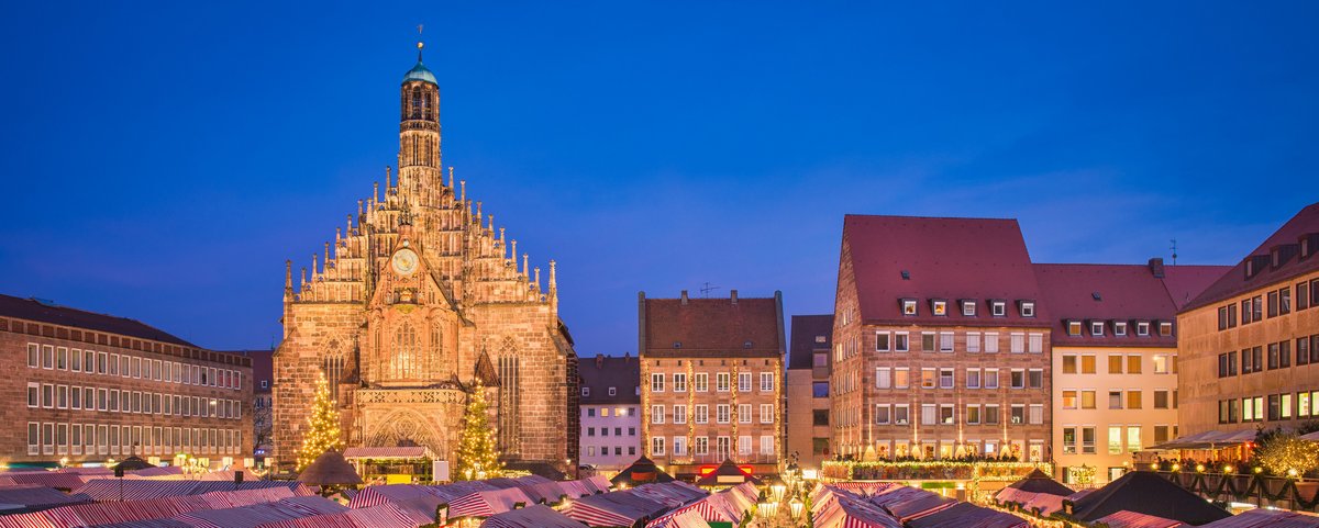 Weihnachtsmarkt in Nürnberg bei Nacht, mit festlich beleuchteten Ständen und einem großen, geschmückten Weihnachtsbaum im Hintergrund.