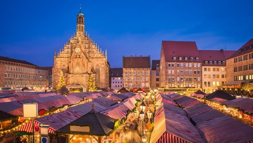 Weihnachtsmarkt in Nürnberg bei Nacht, mit festlich beleuchteten Ständen und einem großen, geschmückten Weihnachtsbaum im Hintergrund.