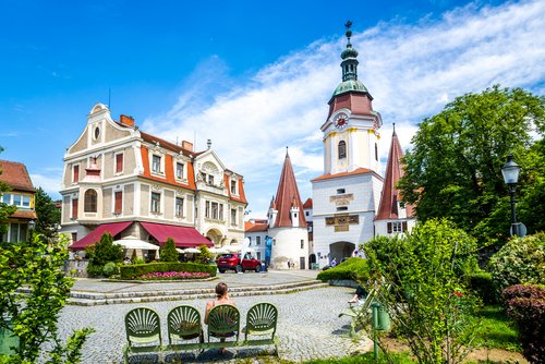 Historisches Stadtzentrum von Krems mit dem Steiner Tor, einem weißen Turm mit Uhr und spitzen Dächern, umgeben von Gebäuden und grünen Bäumen bei blauem Himmel