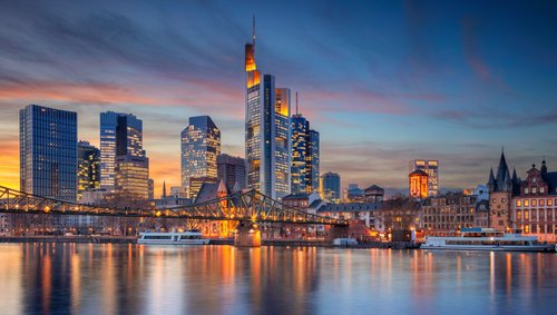 Skyline von Frankfurt am Main mit modernen Hochhäusern und dem Main im Vordergrund bei Sonnenuntergang.