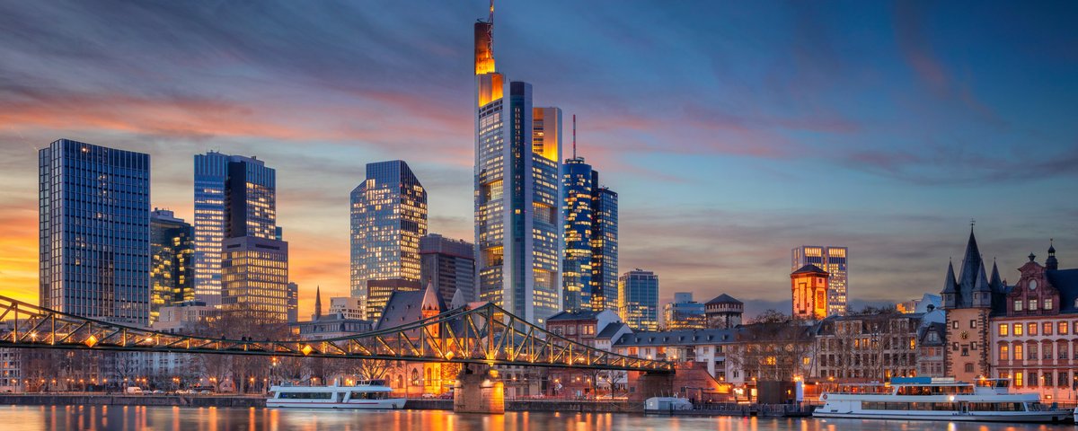 Skyline von Frankfurt am Main mit modernen Hochhäusern und dem Main im Vordergrund bei Sonnenuntergang.