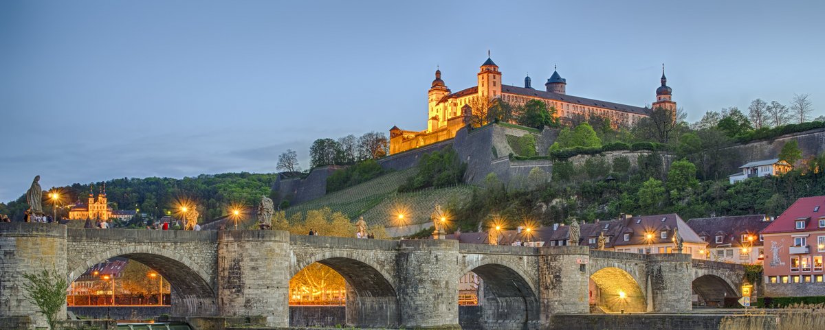 Blick auf die Festung Marienberg in Würzburg, umgeben von grünen Weinbergen und dem Main, bei Abenddämmerung