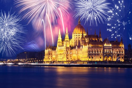 Blick auf das Parlamentsgebäude von Budapest bei Nacht. Es ist gold beleuchtet und über dem Gebäude ist ein Feuerwerk zu sehen.