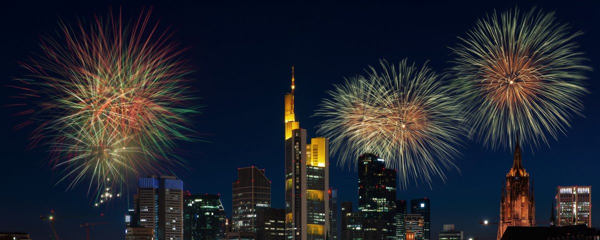 Feuerwerk erleuchtet den Nachthimmel über der Skyline von Frankfurt am Main, mit beleuchteten Wolkenkratzern im Vordergrund.