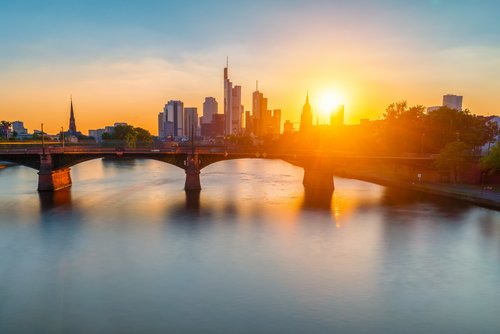 Frankfurter Skyline bei Sonnenuntergang, mit Wolkenkratzern und dem Main, welcher von einer Brücke überspannt wird, im Vordergrund,