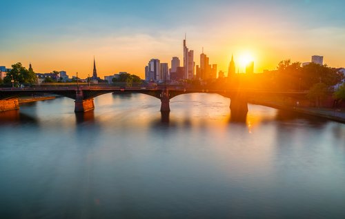 Frankfurter Skyline bei Sonnenuntergang, mit Wolkenkratzern und dem Main, welcher von einer Brücke überspannt wird, im Vordergrund,