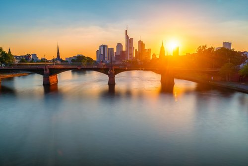 Frankfurter Skyline bei Sonnenuntergang, mit Wolkenkratzern und dem Main, welcher von einer Brücke überspannt wird, im Vordergrund,