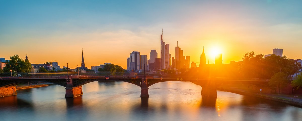 Frankfurter Skyline bei Sonnenuntergang, mit Wolkenkratzern und dem Main, welcher von einer Brücke überspannt wird, im Vordergrund,