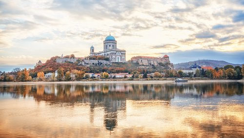 Blick auf die Basilika von Esztergom, Ungarn, mit grüner Kuppel und Donau im Vordergrund, umgeben von herbstlich bunter Landschaft.