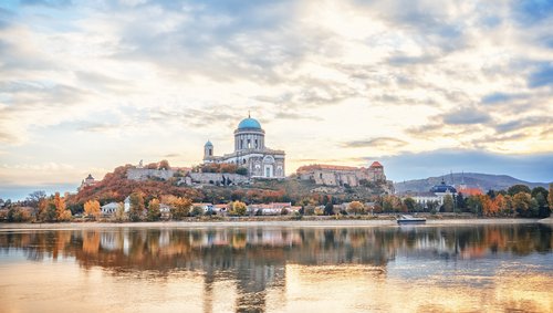Blick auf die Basilika von Esztergom, Ungarn, mit grüner Kuppel und Donau im Vordergrund, umgeben von herbstlich bunter Landschaft.