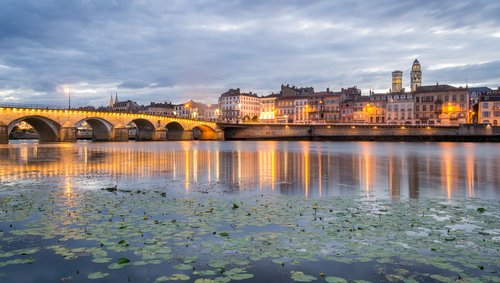 Eine malerische Stadtansicht von Mâcon, Frankreich, mit der Saône im Vordergrund und historischen Gebäuden im Hintergrund bei Abenddämmerung.