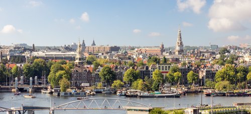 Blick auf Amsterdams Stadtzentrum mit Kanälen, historischen Gebäuden, grünen Bäumen und einer Fußgängerbrücke über das Wasser