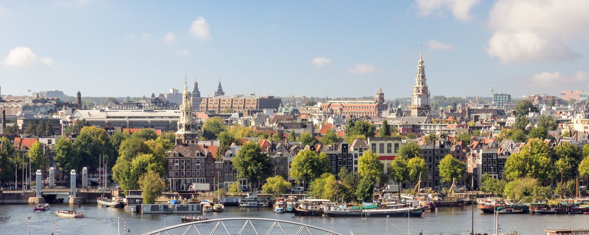 Blick auf Amsterdams Stadtzentrum mit Kanälen, historischen Gebäuden, grünen Bäumen und einer Fußgängerbrücke über das Wasser