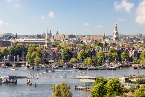 Blick auf Amsterdams Stadtzentrum mit Kanälen, historischen Gebäuden, grünen Bäumen und einer Fußgängerbrücke über das Wasser