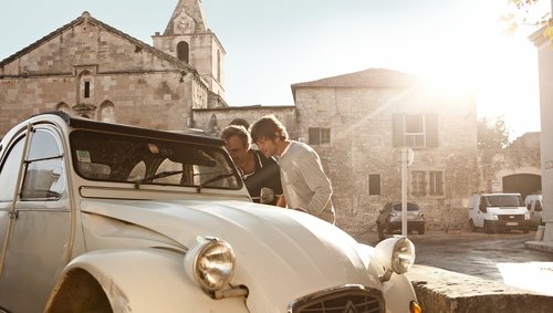 Zwei Männer schauen in der Altstadt von Arles in den Innenraum eines Citroën Oldtimers, umgeben von historischen Gebäuden, die Sonnen geht im Hintergrund langsam unter.