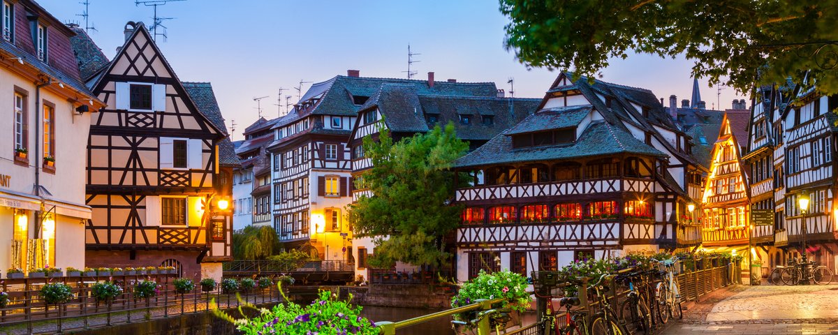 Straßburger Altstadt mit Fachwerkhäusern umgeben von Bäumen und einem Fluss bei Abenddämmerung.