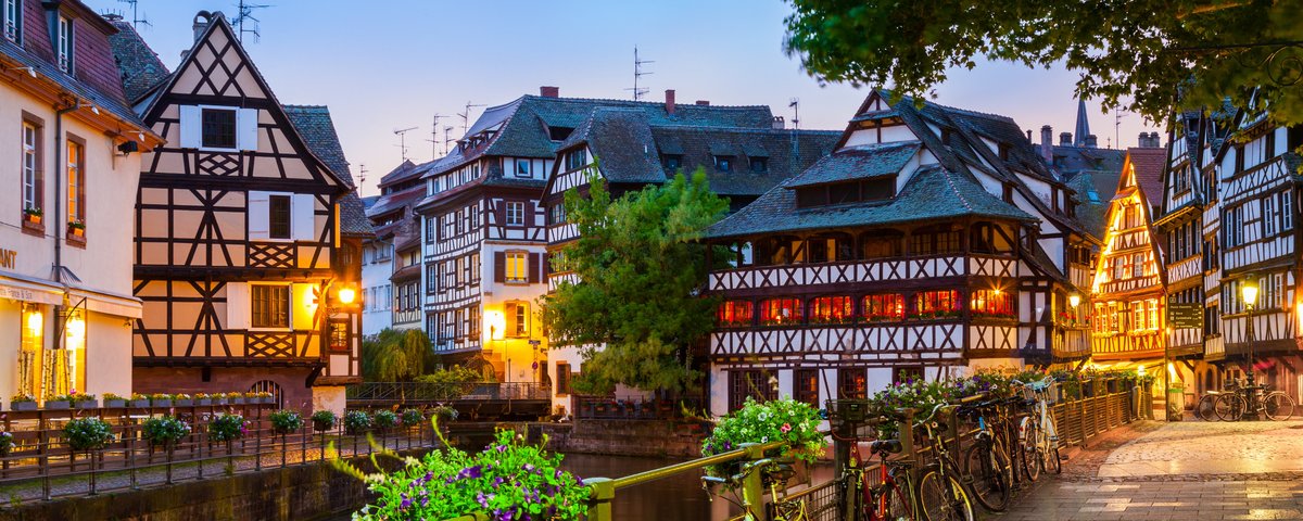 Straßburger Altstadt mit Fachwerkhäusern umgeben von Bäumen und einem Fluss bei Abenddämmerung.