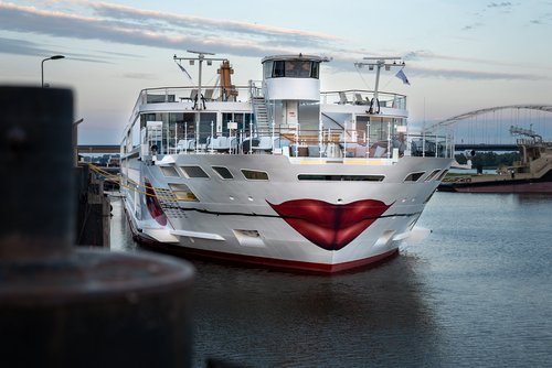 Die A-ROSA SENA mit Kussmund und Rose um Bug liegt am Abend am Anleger in einem Hafen, der Himmel ist leicht bewölkt.