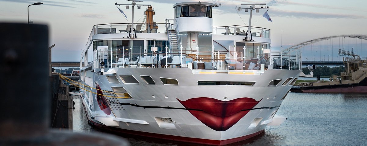 Die A-ROSA SENA mit Kussmund und Rose um Bug liegt am Abend am Anleger in einem Hafen, der Himmel ist leicht bewölkt.