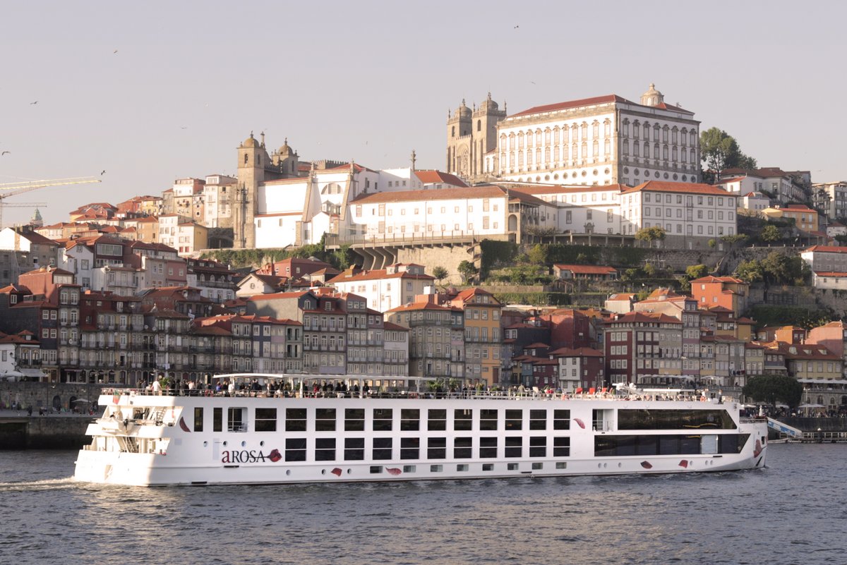 Flusskreuzfahrtschiff A-ROSA ALVA auf dem Douro vor einer Stadt mit historischen Gebäuden und roten Dächern.