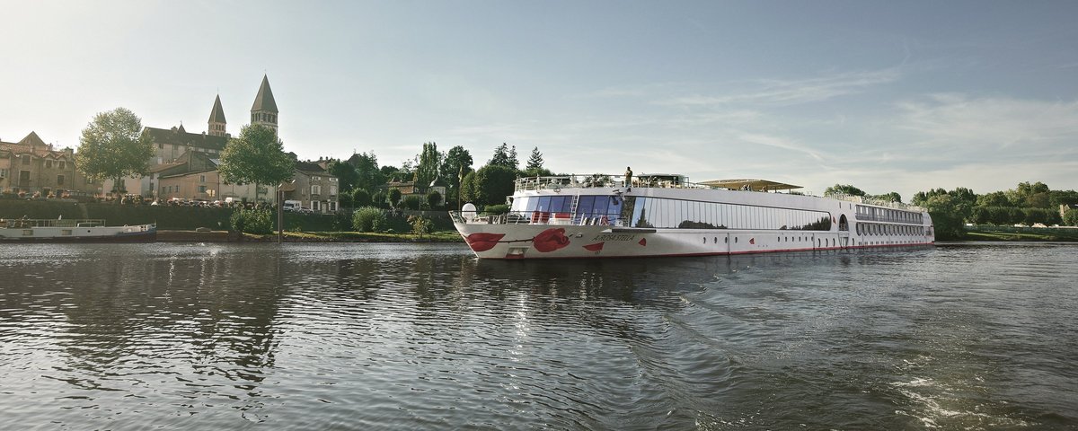 Die A-ROSA STELLA fährt auf einem ruhigen Fluss vor einer Stadt mit historischen Gebäuden und zwei Kirchtürmen bei klarem Himmel.
