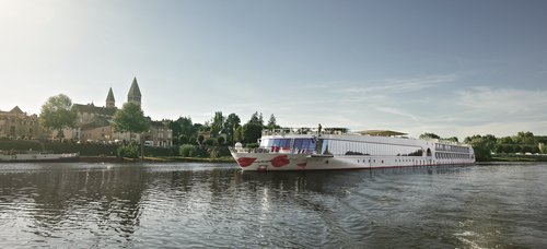 Die A-ROSA STELLA fährt auf einem ruhigen Fluss vor einer Stadt mit historischen Gebäuden und zwei Kirchtürmen bei klarem Himmel.