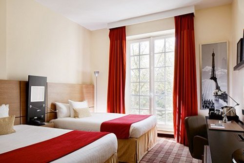 Hotelzimmer mit zwei Einzelbetten, roten Bettläufern, großem Fenster mit roten Vorhängen und einem Bild des Eiffelturms an der Wand.