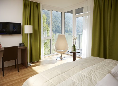 Ein modernes und helles Hotelzimmer im Hotel Wesenufer in Passau an der Donau mit Doppelbett, großen Fenstern, einem Schreibtisch und einem Sessel.