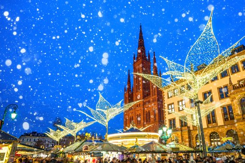 Weihnachtsmarkt in Wiesbaden bei Nacht, mit festlich beleuchteten Ständen und einer Kirche im Hintergrund während es schneit